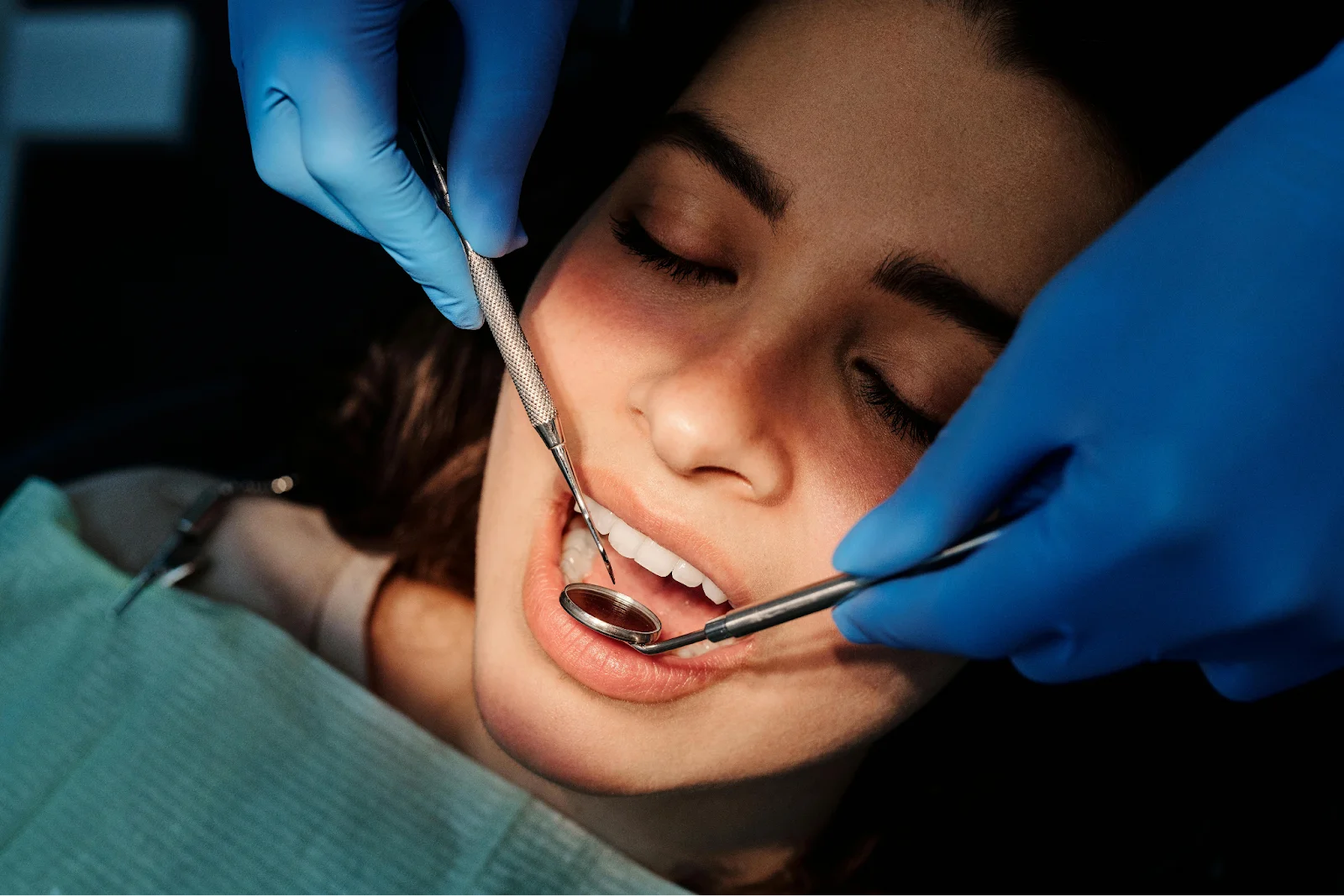 A dentist is using a mirror and a tool to examine a woman's teeth
