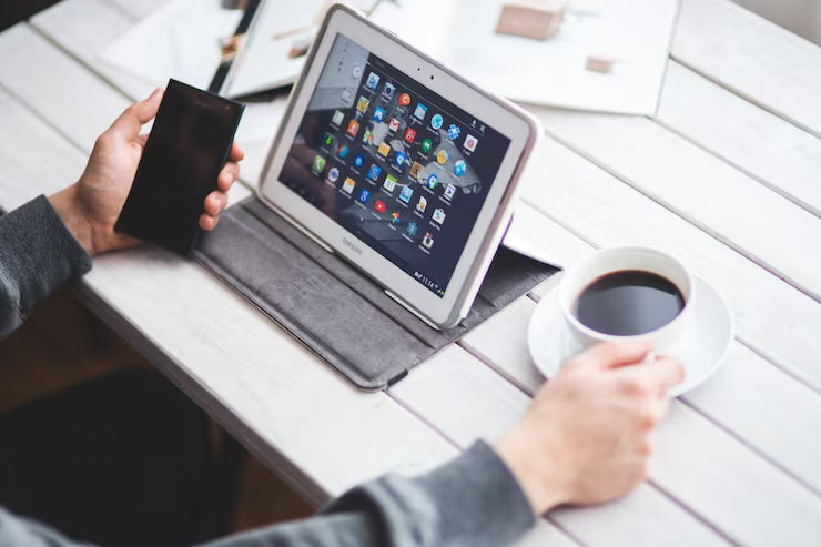 Person holding a smartphone beside a tablet on a desk